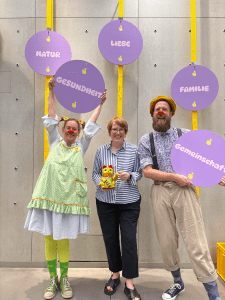 Clownin Lakritze, Anja Krüger von der Volksbank und Clown Welle präsentieren ein Mitmach-Tool der aktuellen Ausstellung Lebenselixier Glück - von und mit Dr. Clown